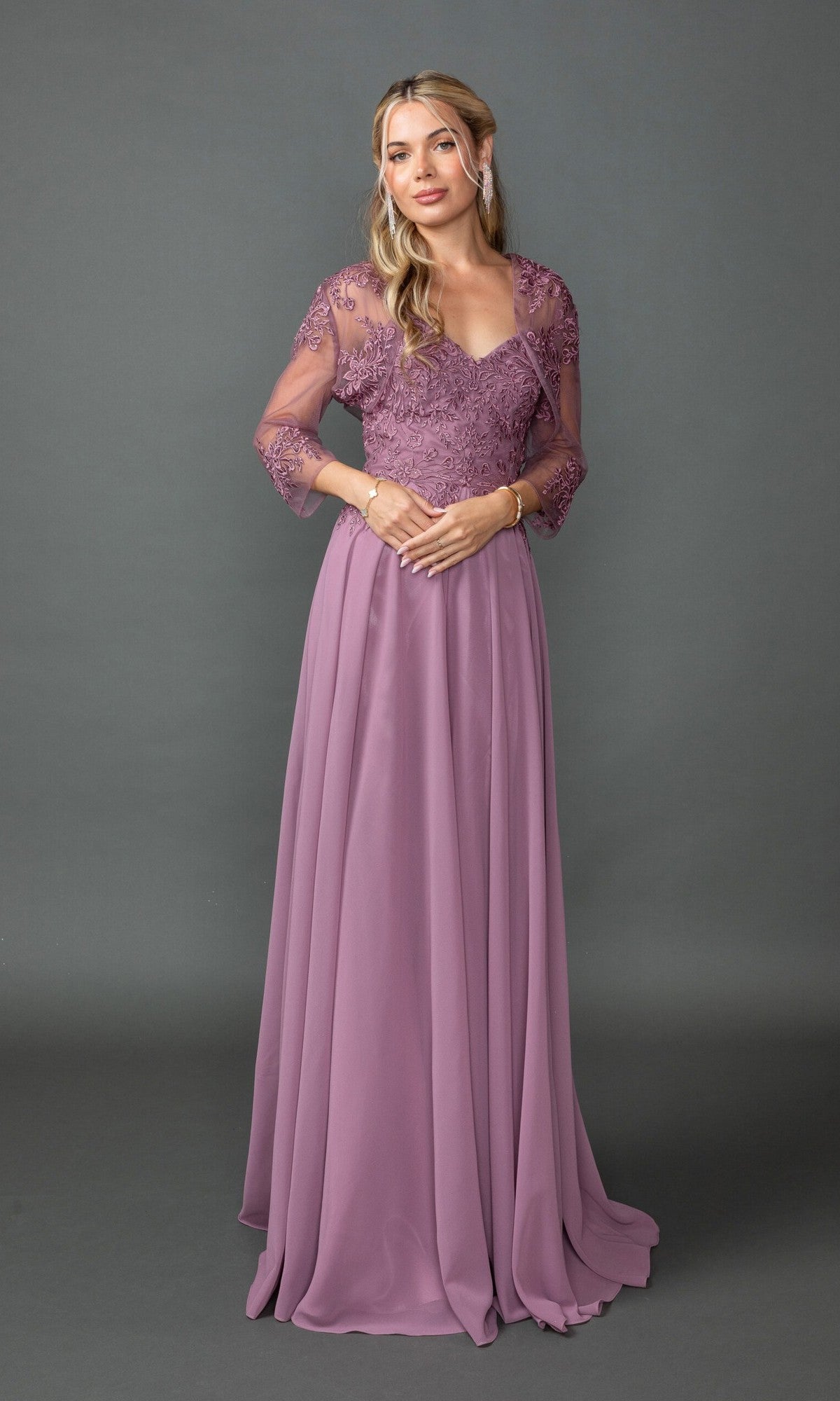 A woman models the Dancing Queen 4542 long prom dress in mauve, with lace-embroidered sleeves and a fitted bodice, standing before a plain gray backdrop.